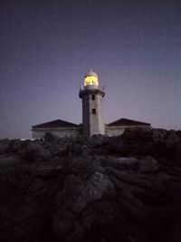 Low angle view of lighthouse by building against sky at dusk