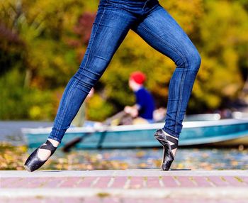 Low section of woman wearing ballet shoes dancing against boat on lake