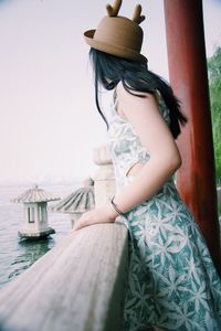 Side view of woman wearing hat while standing at beach against clear sky