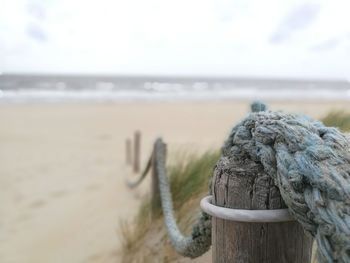 Close-up of rope tied to wooden post at beach against sky