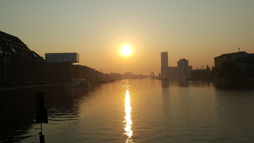 Buildings by river against sky during sunset