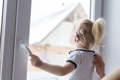 Rear view of deaf girl looking through window