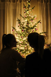 Rear view of friends by illuminated christmas tree at home