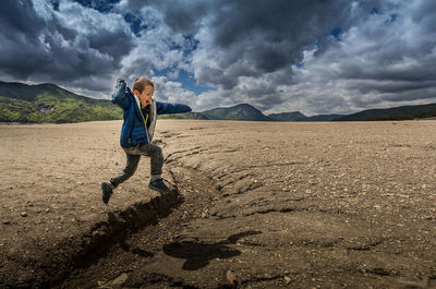 Full length of boy on landscape against cloudy sky