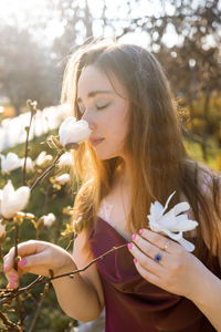Young blonde woman enjoys by blooming magnolia tree
