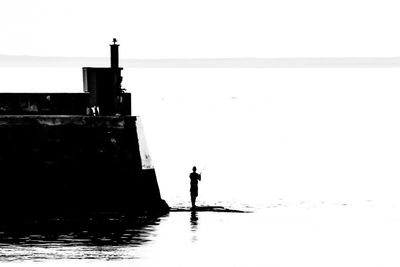 Silhouette man standing by sea against clear sky