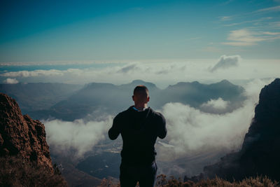 Rear view of man standing on mountain against sky