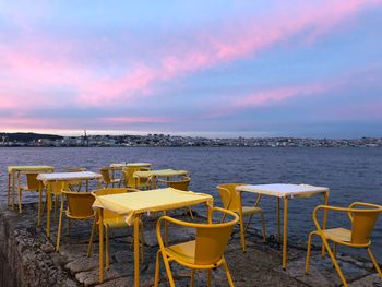 Chairs and tables on beach against sky during sunset