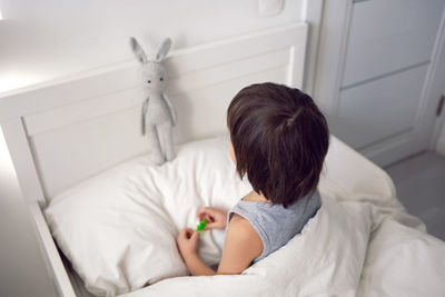 Child boy lies in a white children's bed with a blanket in a room with toys rabbits