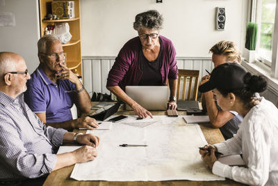 Female instructor explaining senior men and woman over map at table during navigation course