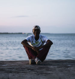 Portrait of man sitting at beach against sky during sunset