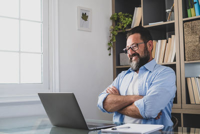 Smiling man looking at laptop against bookshelf