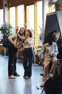 Smiling teenage girl taking selfie through smart phone with female friend in school