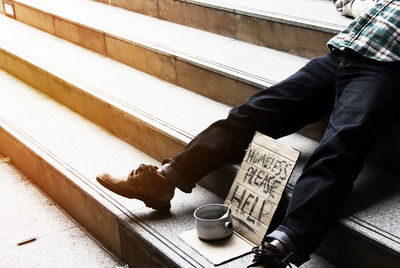 Low section of man sitting on steps with text on cardboard