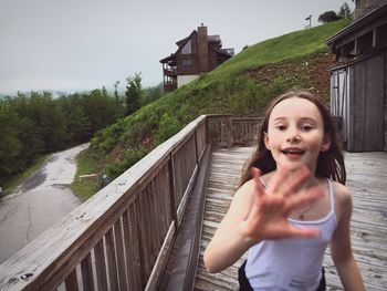 Portrait of smiling girl gesturing on wooden footbridge 