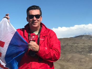 Portrait of man in sunglasses holding flag against sky