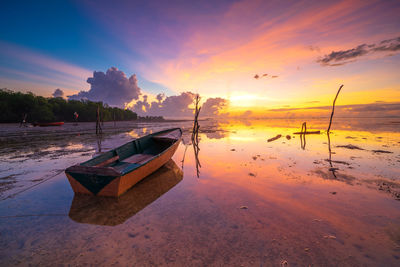 Boat moored on shore against sky during sunset