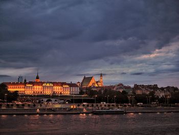 River by illuminated buildings against sky at dusk