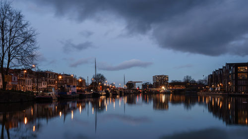 Calm lake against sky in city at dusk