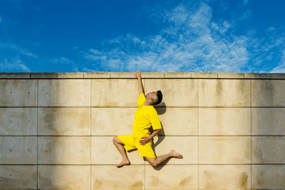 Man hanging on wall with one hand during sunny day