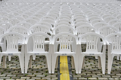 Rows of white plastic chairs on a cobblestone pavement with a cable tray