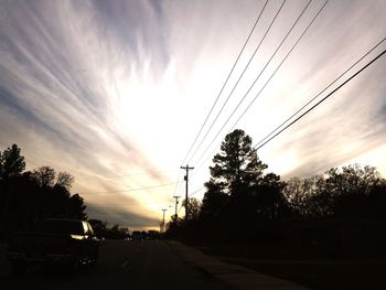 Silhouette trees by road against sky during sunset