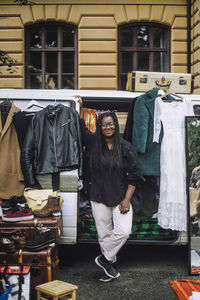 Smiling female owner standing near van while selling goods during second hand sale at flea market