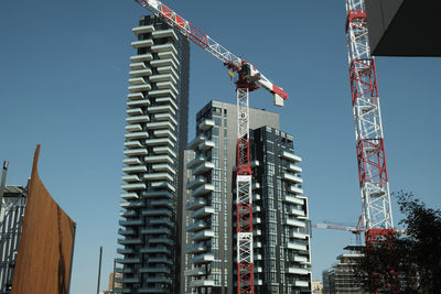 Low angle view of crane and buildings against clear sky