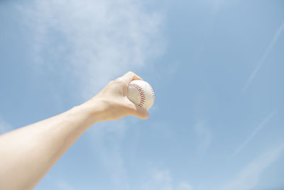 Cropped hand holding baseball against sky