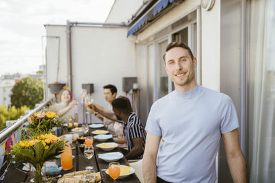 Portrait of smiling man with friends enjoying during dinner party in balcony