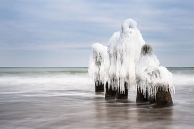 Panoramic view of wooden posts in sea against sky