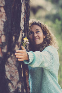 Young woman standing against tree trunk