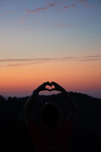 Silhouette woman with heart shape against sky during sunset