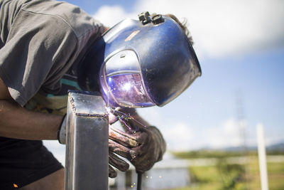 Close up view of man welding outdoors on rooftop.