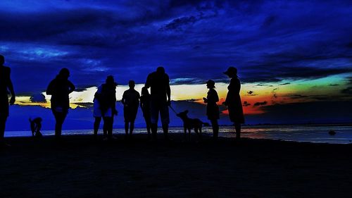 Silhouette of people at beach against cloudy sky