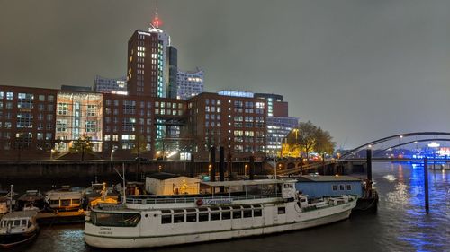 Boats in river by illuminated buildings against sky at night