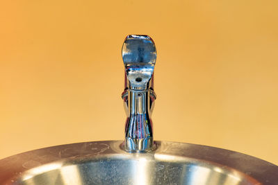 Close-up of drinking fountain against yellow background