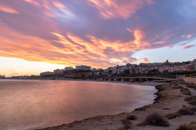 River by buildings against sky during sunset