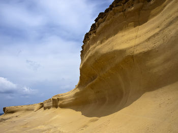 Low angle view of sand dunes against cloudy sky