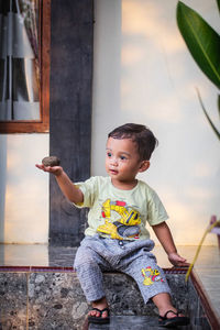 Cute boy looking away while sitting on wall