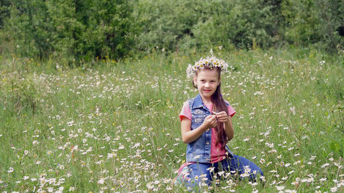 On a chamomile lawn, a sweet girl in a wreath of chamomiles, looks at the daisy, cuts off the petals