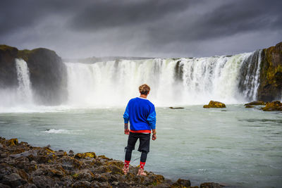 Rear view of man standing against waterfall