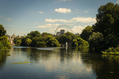 View of ferris wheel by river against sky