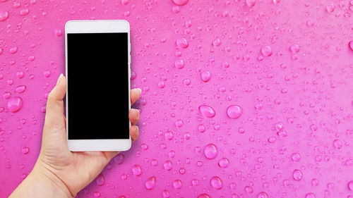 Cropped hand of woman holding smart phone over wet table