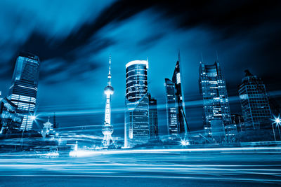 Light trails on street by buildings against sky at night