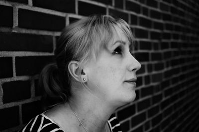 Close-up of thoughtful woman sitting by brick wall