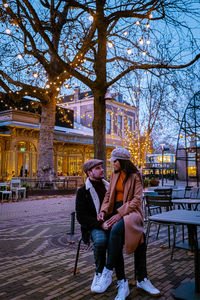 Couple sitting on chair in illuminated city at dusk
