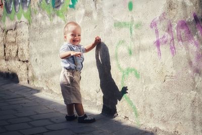 Full length portrait of a smiling young man standing against wall
