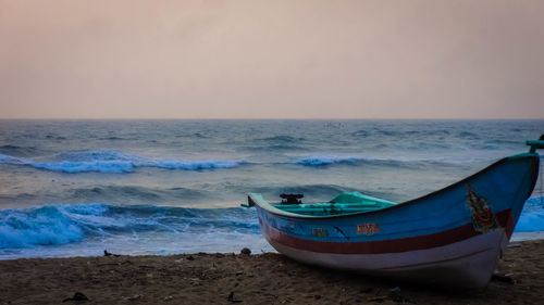 Boat moored at beach against sky at dusk