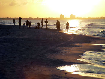 Silhouette people at beach against sky during sunset